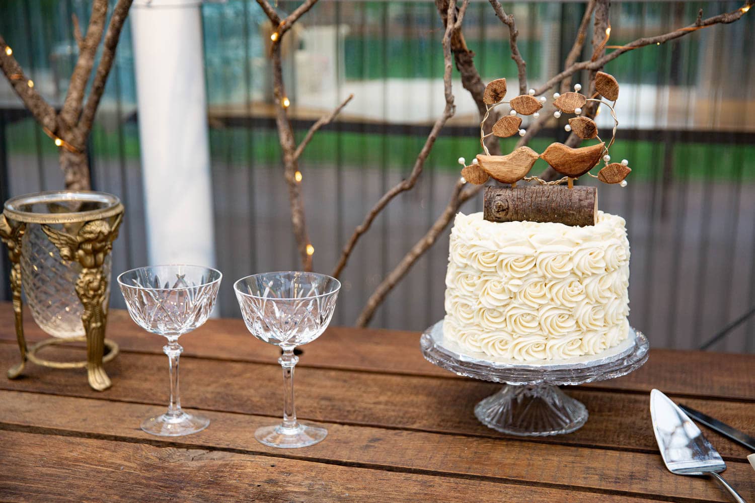Rustic cake table set up at Black Diamond Gardens with a small wedding cake covered in ivory buttercream roses with vintage champagne glasses.