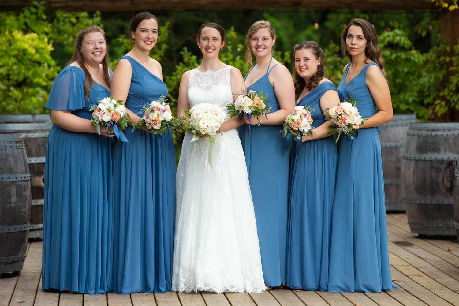 A bride poses with her bridesmaids, each wearing a customized blue maxi dress different from all the rest.