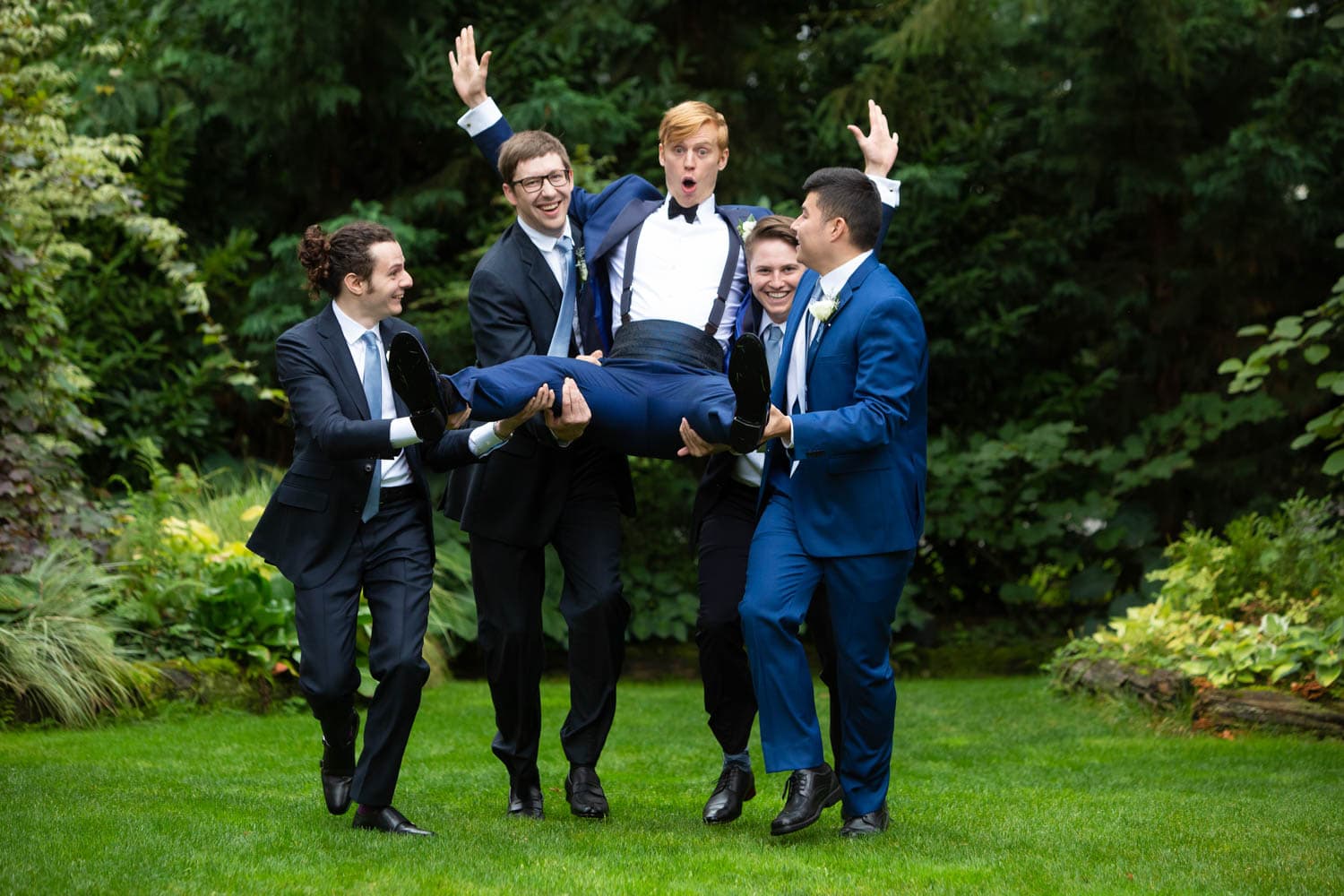 The groom goofs off with his groomsmen as they pick him up off the ground.