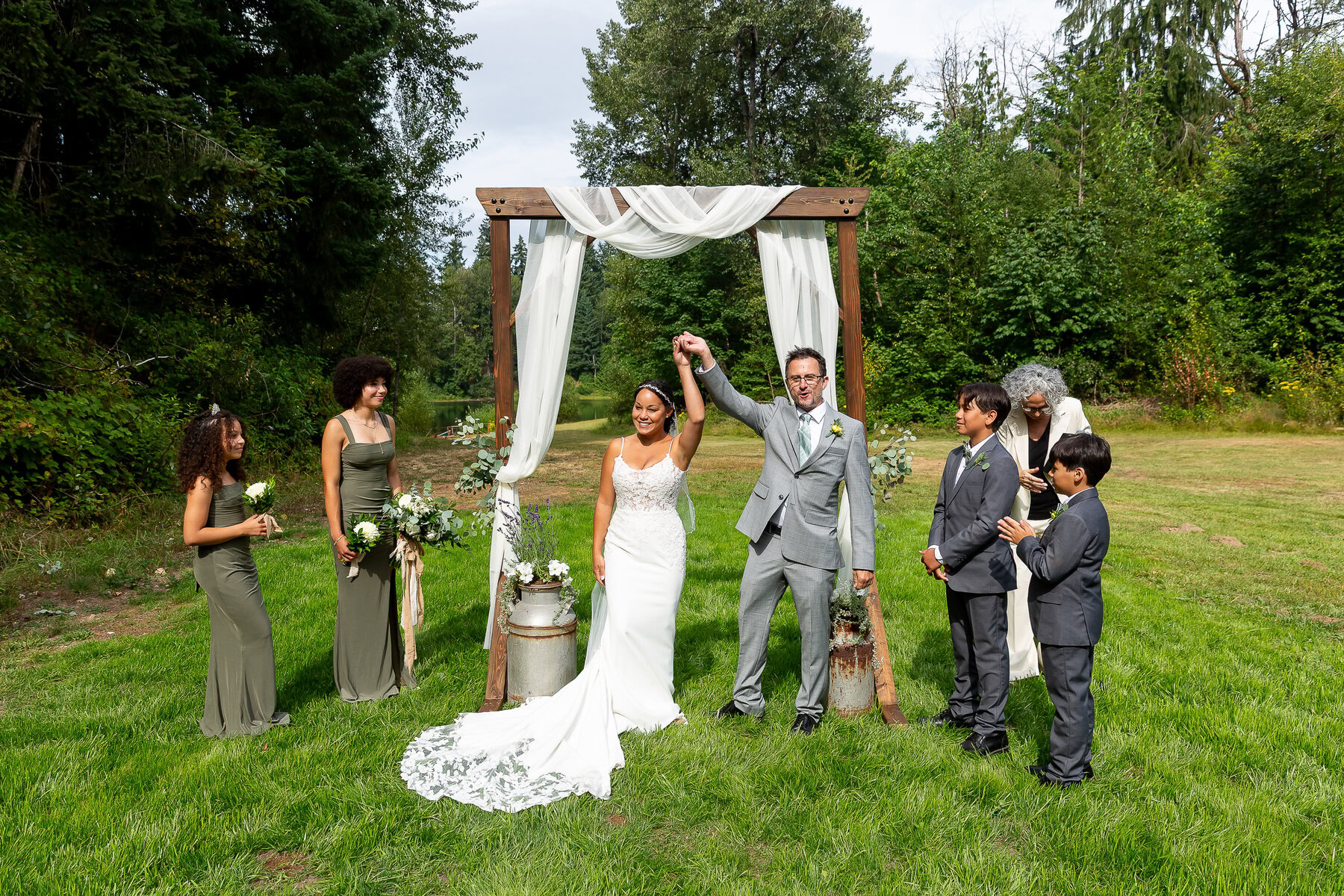 Wedding ceremony outdoor photography by Nallayer Studios, with bride and groom celebrating under rustic wooden arch.