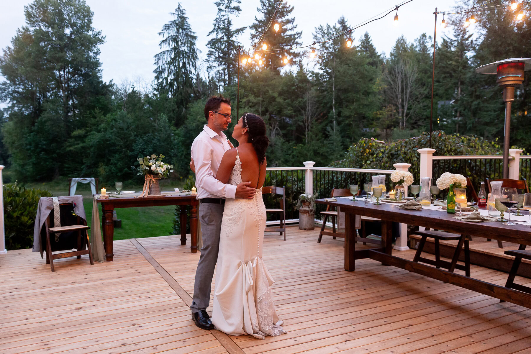 Outdoor wedding reception on wooden deck with romantic ambiance and string lights.